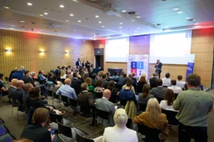 Vue d'ensemble de la salle de conférence des Trophées MOCI, avec un intervenant au pupitre et l'audience attentive.