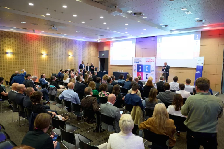 Vue d'ensemble de la salle de conférence des Trophées MOCI, avec un intervenant au pupitre et l'audience attentive.